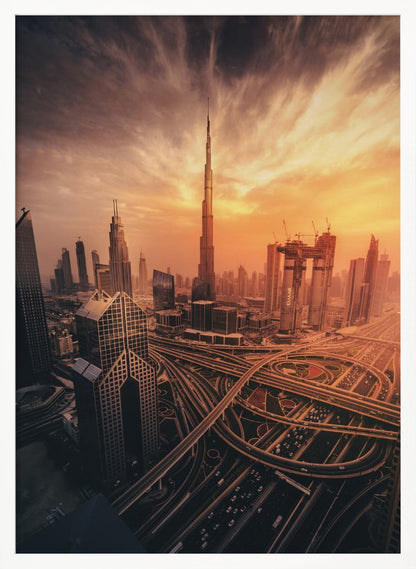 A dramatic high-angle photograph of the Dubai skyline at sunset. The Burj Khalifa stands tall in the center, bathed in the warm light of the setting sun, while a complex network of highways and interchanges weaves between modern skyscrapers in the foreground under a cloudy, orange-tinted sky. Poster