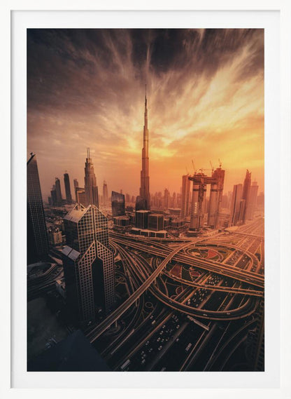 A dramatic high-angle photograph of the Dubai skyline at sunset. The Burj Khalifa stands tall in the center, bathed in the warm light of the setting sun, while a complex network of highways and interchanges weaves between modern skyscrapers in the foreground under a cloudy, orange-tinted sky. Poster