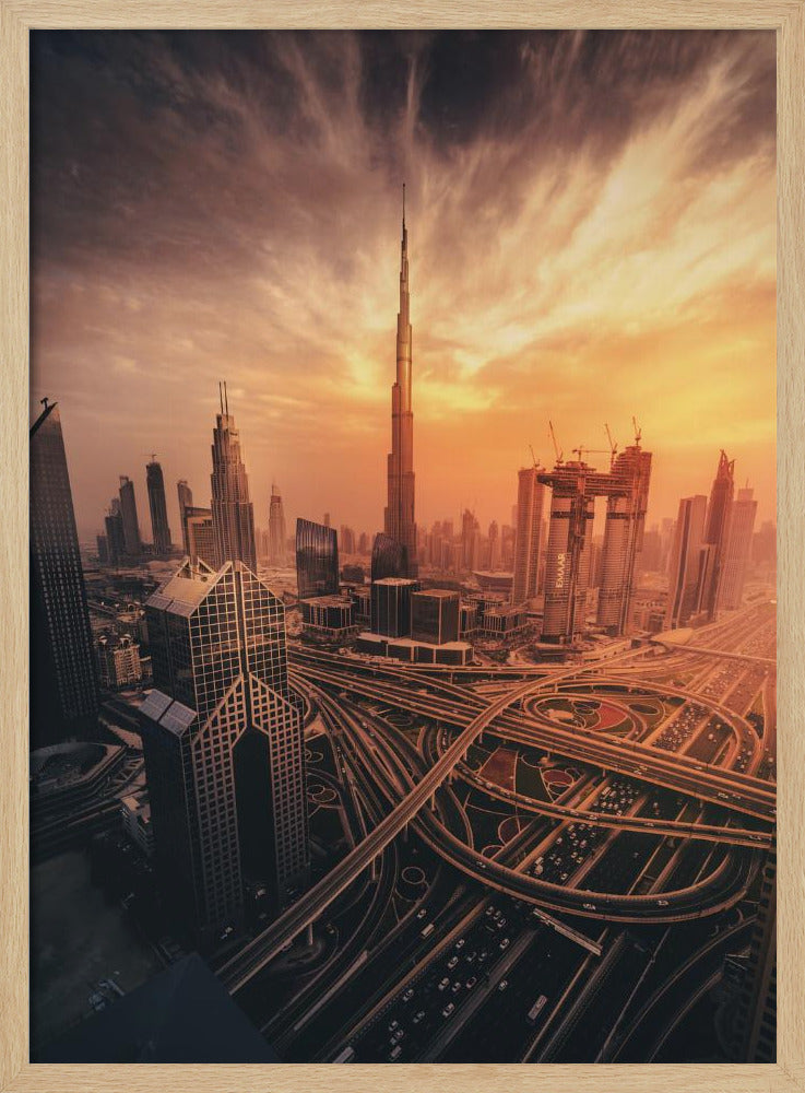 A dramatic high-angle photograph of the Dubai skyline at sunset. The Burj Khalifa stands tall in the center, bathed in the warm light of the setting sun, while a complex network of highways and interchanges weaves between modern skyscrapers in the foreground under a cloudy, orange-tinted sky. Poster