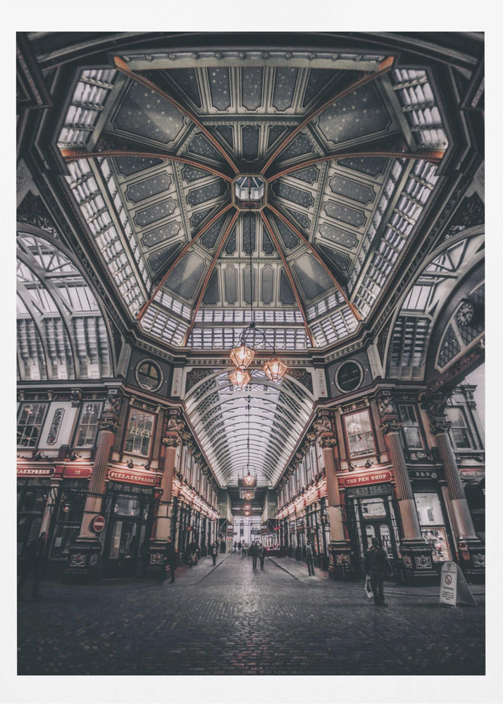 A wide-angle, symmetrical photograph looking down the center of an ornate Victorian covered market, Leadenhall Market. The focus is on the elaborate, arched glass and ironwork ceiling which is decorated in dark blue with gold stars. Below, a cobblestone path is lined with traditional shops with glowing lights, and a few people can be seen walking in the distance. The image has a moody, high-contrast aesthetic. Wall Art