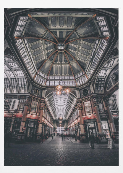A wide-angle, symmetrical photograph looking down the center of an ornate Victorian covered market, Leadenhall Market. The focus is on the elaborate, arched glass and ironwork ceiling which is decorated in dark blue with gold stars. Below, a cobblestone path is lined with traditional shops with glowing lights, and a few people can be seen walking in the distance. The image has a moody, high-contrast aesthetic. Wall Art