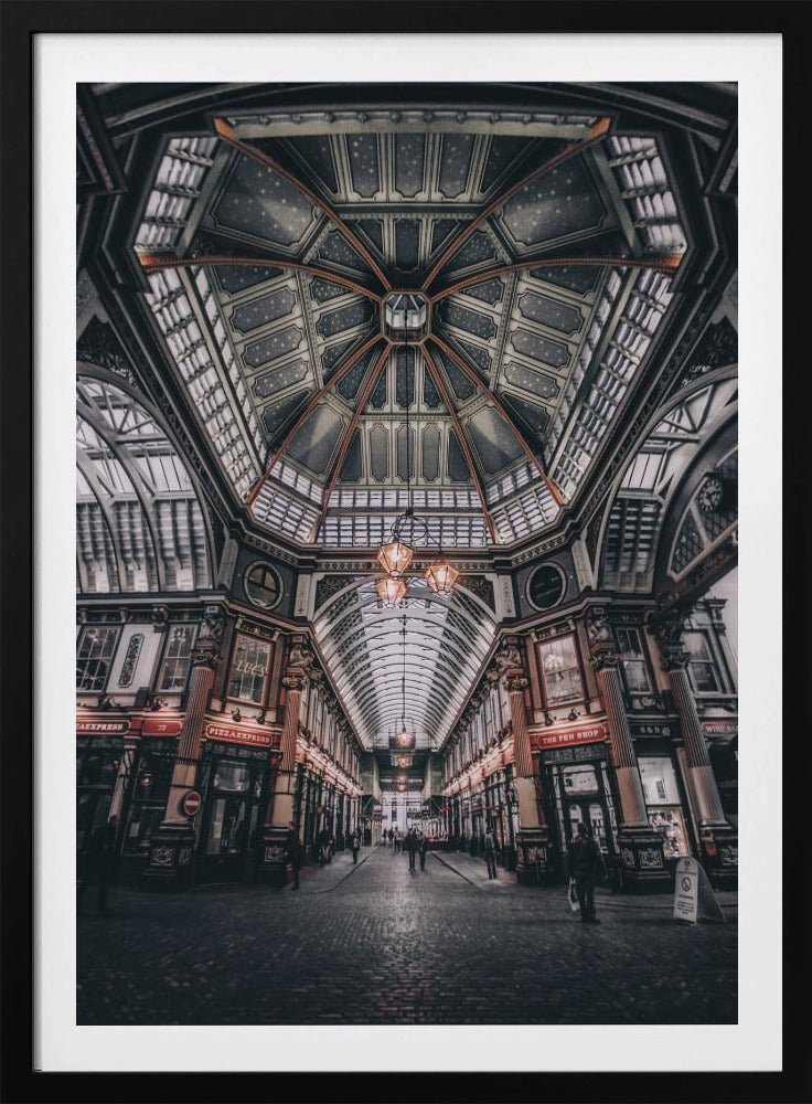 A wide-angle, symmetrical photograph looking down the center of an ornate Victorian covered market, Leadenhall Market. The focus is on the elaborate, arched glass and ironwork ceiling which is decorated in dark blue with gold stars. Below, a cobblestone path is lined with traditional shops with glowing lights, and a few people can be seen walking in the distance. The image has a moody, high-contrast aesthetic. Wall Art
