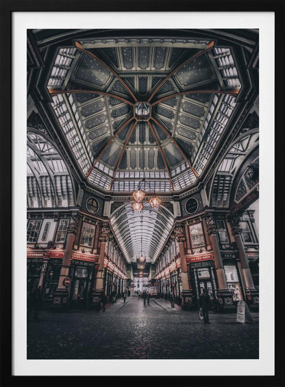 A wide-angle, symmetrical photograph looking down the center of an ornate Victorian covered market, Leadenhall Market. The focus is on the elaborate, arched glass and ironwork ceiling which is decorated in dark blue with gold stars. Below, a cobblestone path is lined with traditional shops with glowing lights, and a few people can be seen walking in the distance. The image has a moody, high-contrast aesthetic. Wall Art