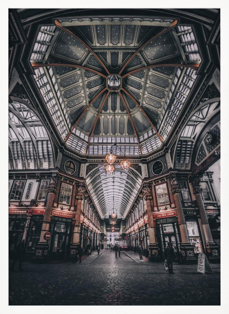 A wide-angle, symmetrical photograph looking down the center of an ornate Victorian covered market, Leadenhall Market. The focus is on the elaborate, arched glass and ironwork ceiling which is decorated in dark blue with gold stars. Below, a cobblestone path is lined with traditional shops with glowing lights, and a few people can be seen walking in the distance. The image has a moody, high-contrast aesthetic. Wall Art