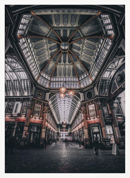A wide-angle, symmetrical photograph looking down the center of an ornate Victorian covered market, Leadenhall Market. The focus is on the elaborate, arched glass and ironwork ceiling which is decorated in dark blue with gold stars. Below, a cobblestone path is lined with traditional shops with glowing lights, and a few people can be seen walking in the distance. The image has a moody, high-contrast aesthetic. Wall Art
