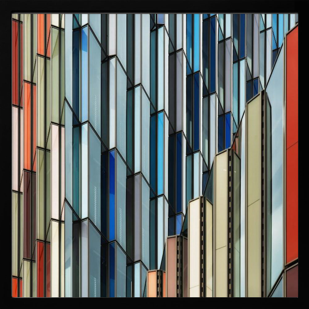 A close-up abstract photograph of a modern building's facade, featuring a complex pattern of colorful, angular glass panels in shades of blue, orange, red, and gray, all presented within a light wood frame. Wall Art