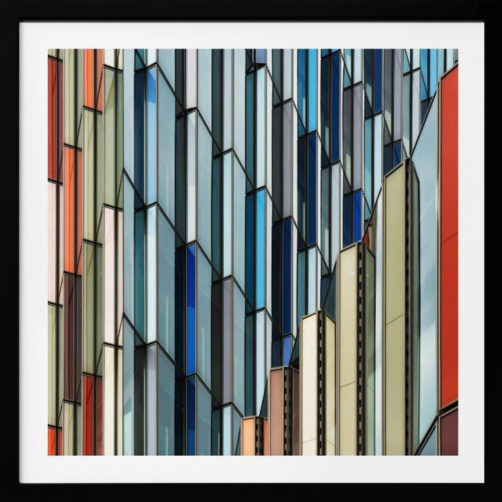 A close-up abstract photograph of a modern building's facade, featuring a complex pattern of colorful, angular glass panels in shades of blue, orange, red, and gray, all presented within a light wood frame. Wall Art