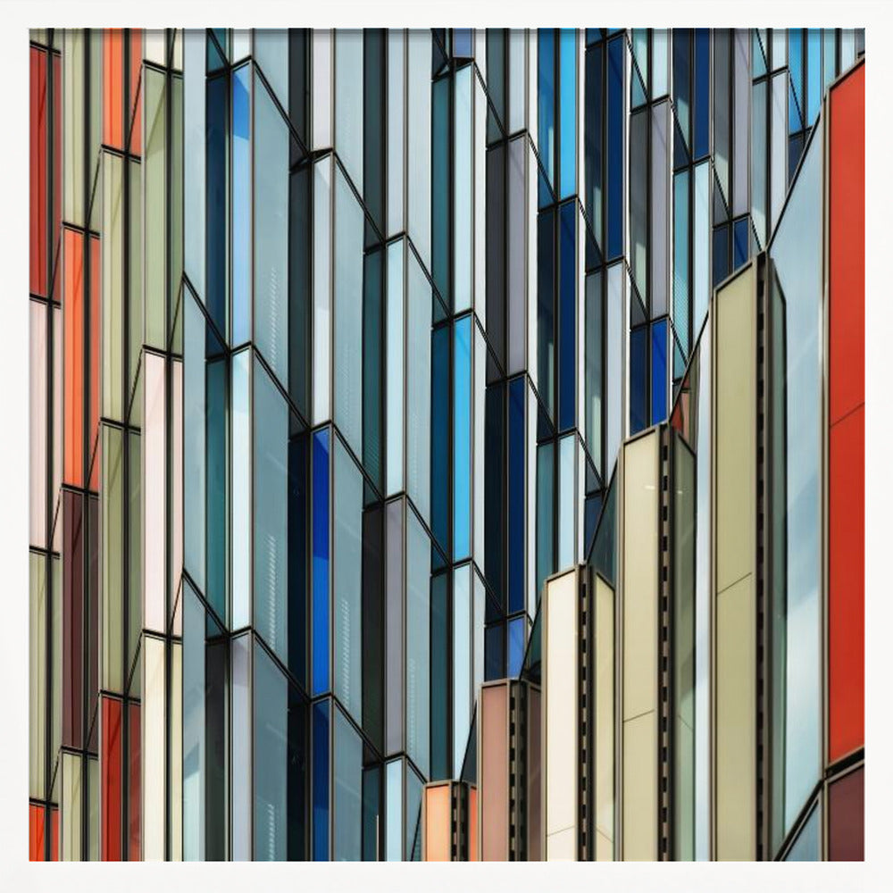 A close-up abstract photograph of a modern building's facade, featuring a complex pattern of colorful, angular glass panels in shades of blue, orange, red, and gray, all presented within a light wood frame. Wall Art