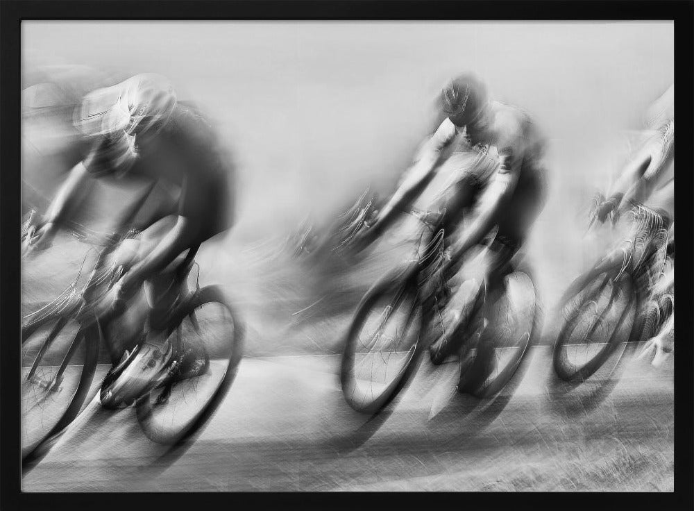 A dynamic black and white action photograph of three cyclists racing, captured with a slow shutter speed to create a dramatic motion blur effect. The riders and their bikes are blurred into streaks of light and shadow, conveying a powerful sense of speed and intensity. The image is presented within a silver-toned frame. Poster