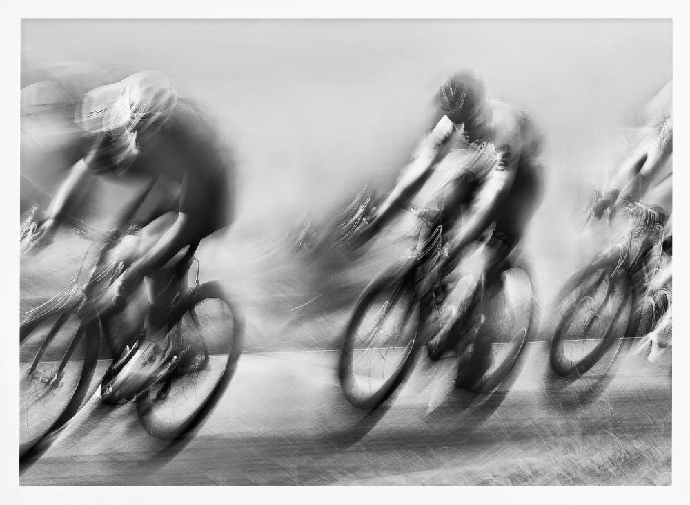 A dynamic black and white action photograph of three cyclists racing, captured with a slow shutter speed to create a dramatic motion blur effect. The riders and their bikes are blurred into streaks of light and shadow, conveying a powerful sense of speed and intensity. The image is presented within a silver-toned frame. Poster