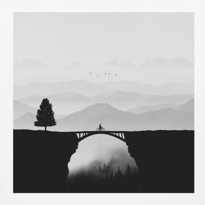 A minimalist black and white artwork featuring the silhouette of a cyclist crossing a high arched bridge between two cliffs. A lone tree stands on one cliff, while layers of misty mountains fill the background, creating a sense of depth and solitude. Poster