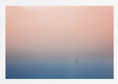 A minimalist framed photograph of a solitary person on a stand-up paddleboard, silhouetted against a vast, calm expanse of water under a hazy, gradient sky that shifts from soft pink to deep blue. Wall Art