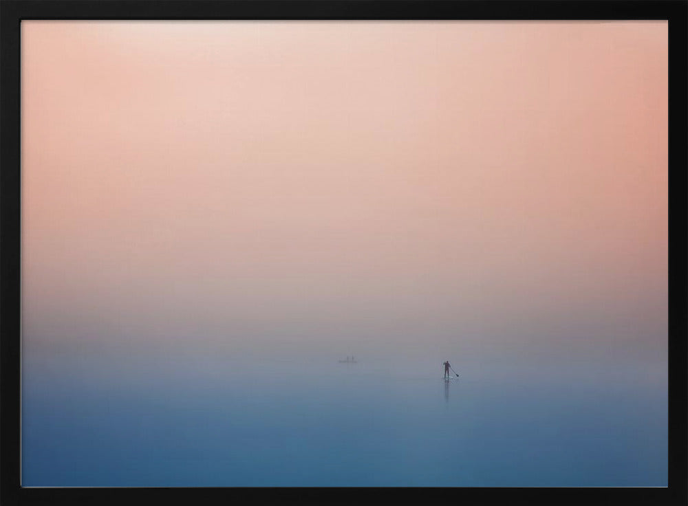 A minimalist framed photograph of a solitary person on a stand-up paddleboard, silhouetted against a vast, calm expanse of water under a hazy, gradient sky that shifts from soft pink to deep blue. Wall Art
