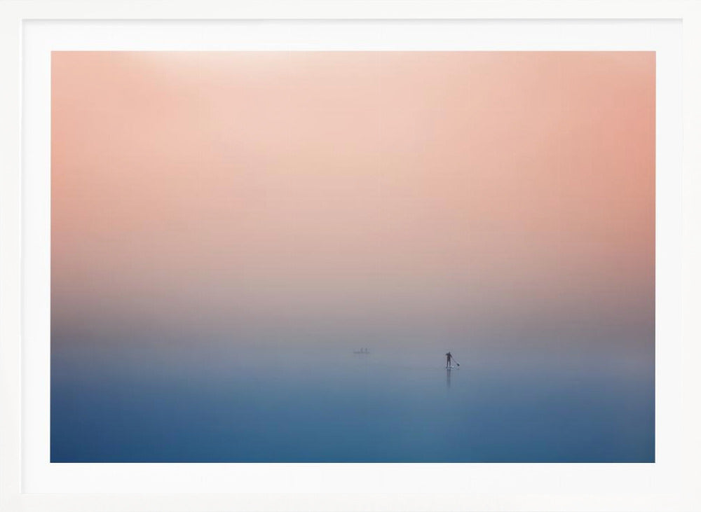 A minimalist framed photograph of a solitary person on a stand-up paddleboard, silhouetted against a vast, calm expanse of water under a hazy, gradient sky that shifts from soft pink to deep blue. Wall Art
