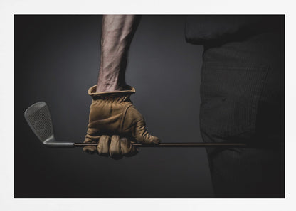A dramatic close-up of a person's muscular forearm and hand wearing a tan leather glove, holding a golf iron horizontally against a dark background, framed in silver. Wall Art