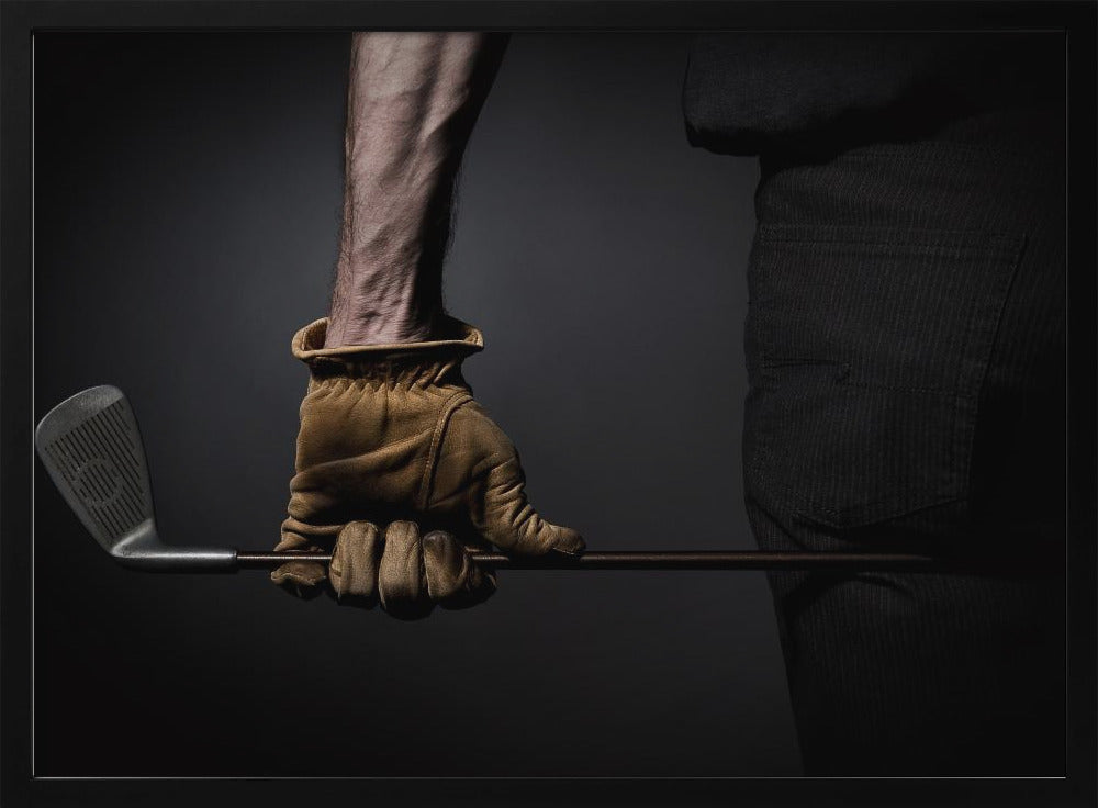 A dramatic close-up of a person's muscular forearm and hand wearing a tan leather glove, holding a golf iron horizontally against a dark background, framed in silver. Wall Art