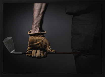 A dramatic close-up of a person's muscular forearm and hand wearing a tan leather glove, holding a golf iron horizontally against a dark background, framed in silver. Wall Art