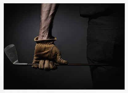 A dramatic close-up of a person's muscular forearm and hand wearing a tan leather glove, holding a golf iron horizontally against a dark background, framed in silver. Wall Art