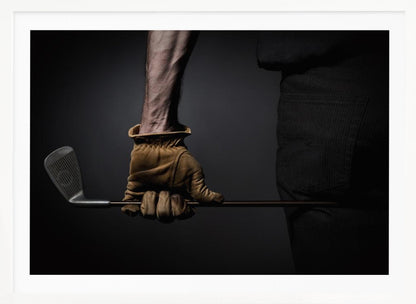 A dramatic close-up of a person's muscular forearm and hand wearing a tan leather glove, holding a golf iron horizontally against a dark background, framed in silver. Wall Art