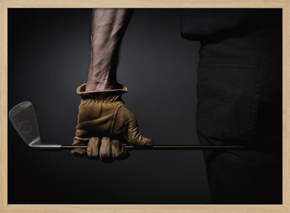 A dramatic close-up of a person's muscular forearm and hand wearing a tan leather glove, holding a golf iron horizontally against a dark background, framed in silver. Wall Art