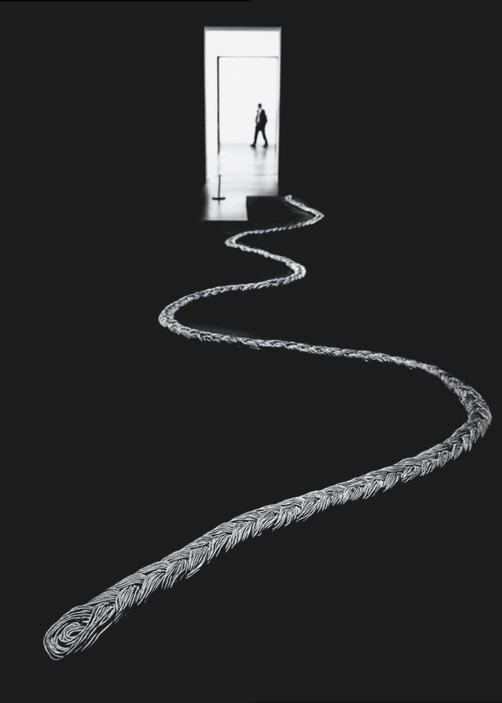 A high-contrast, black and white photograph of a thick, silver, braided rope winding across a black floor, leading towards a brightly lit doorway in the distance where a silhouetted man is walking away. Wall Art