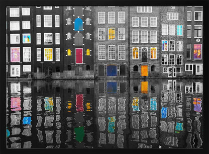 A framed black and white photograph of canal houses in Amsterdam, with selective coloring highlighting windows and doors in vibrant shades of red, blue, yellow, and pink. The colorful architectural details are mirrored in the rippling water of the canal below. Artwork