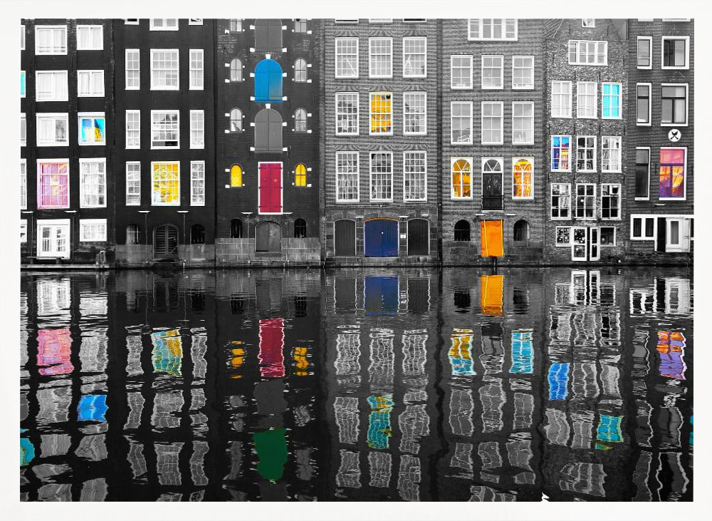 A framed black and white photograph of canal houses in Amsterdam, with selective coloring highlighting windows and doors in vibrant shades of red, blue, yellow, and pink. The colorful architectural details are mirrored in the rippling water of the canal below. Artwork