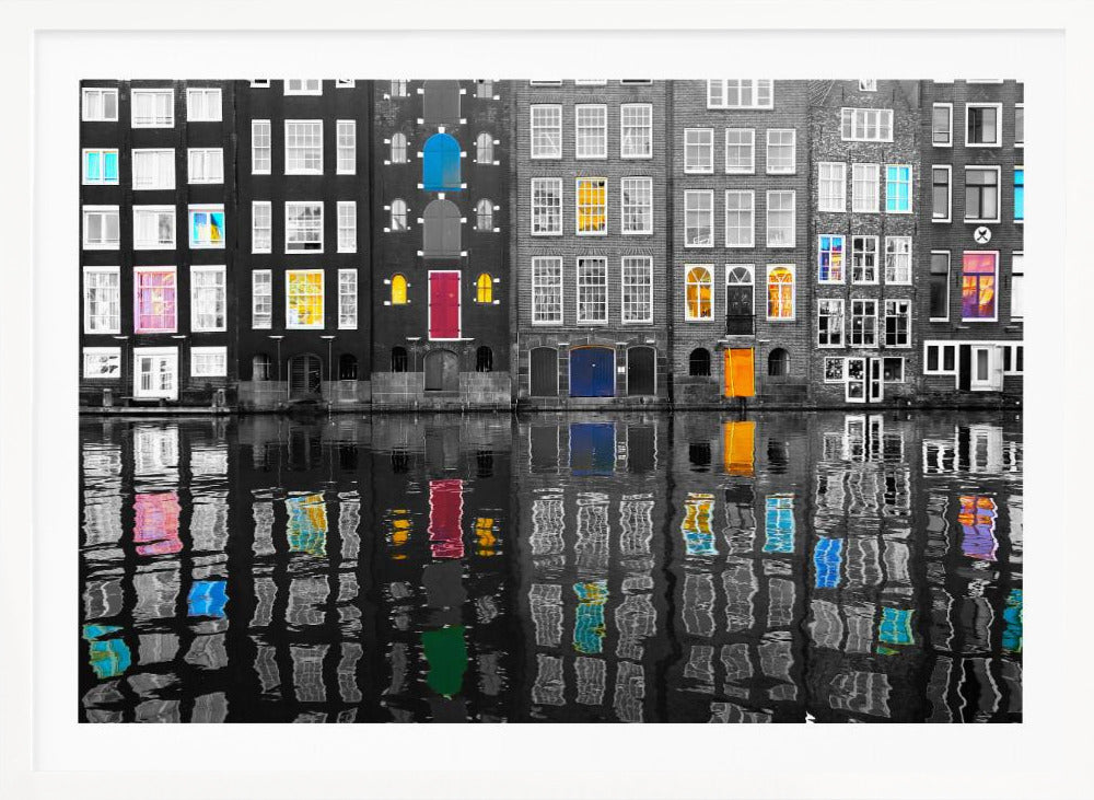 A framed black and white photograph of canal houses in Amsterdam, with selective coloring highlighting windows and doors in vibrant shades of red, blue, yellow, and pink. The colorful architectural details are mirrored in the rippling water of the canal below. Artwork