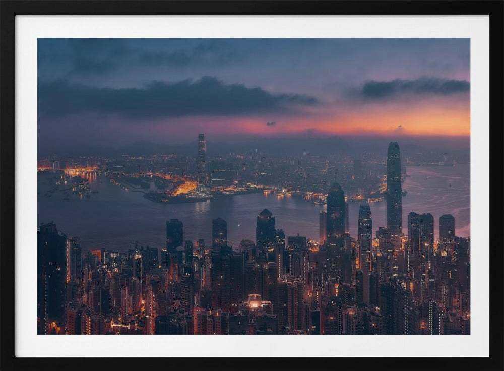 An aerial photograph of a sprawling city skyline at dusk, likely Hong Kong, with countless illuminated skyscrapers. The sky above transitions from a warm orange glow at the horizon to a deep purple, with dark clouds overhead. The city lights cast a golden reflection on the water of the harbor. The entire image is presented within a silver-colored frame. Poster