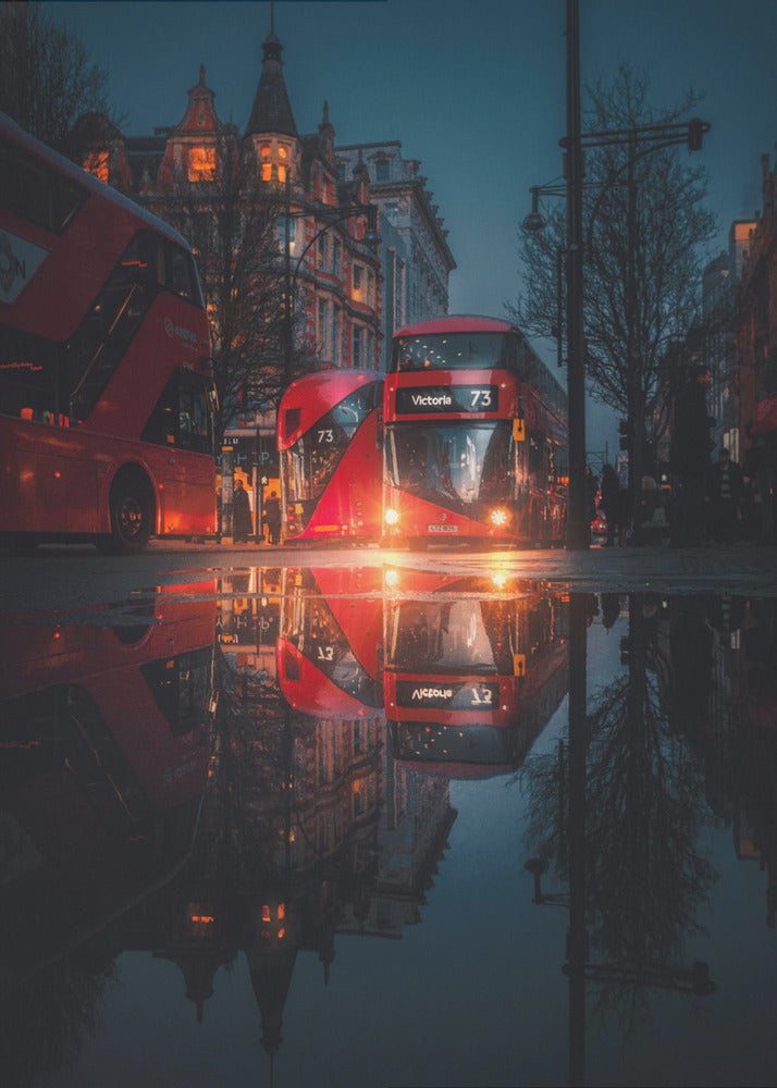 A moody, low-angle photograph of a wet London street at dusk, with a vibrant red double-decker bus reflected perfectly in a large puddle in the foreground. Print