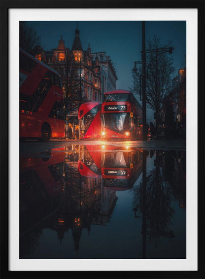 A moody, low-angle photograph of a wet London street at dusk, with a vibrant red double-decker bus reflected perfectly in a large puddle in the foreground. Print