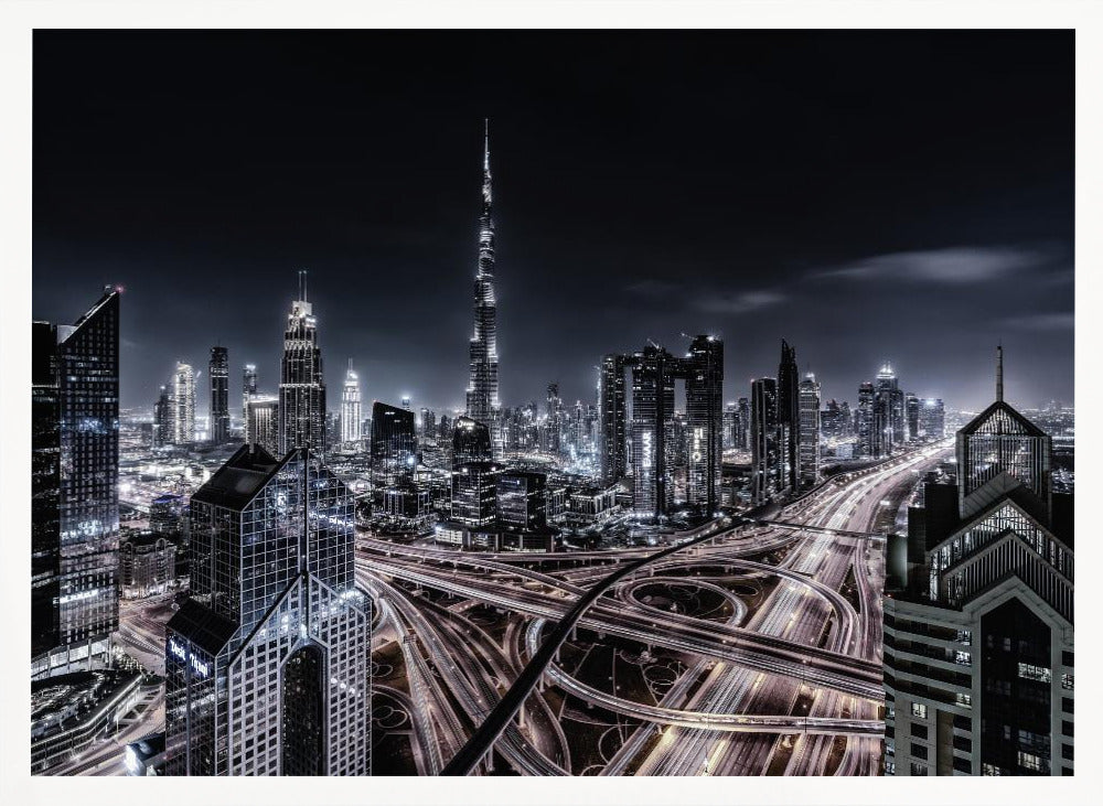 A striking black and white aerial photograph of the Dubai skyline at night, captured in a silver frame. The Burj Khalifa stands tall in the background, while a complex web of illuminated highway overpasses and light trails from traffic fills the foreground, creating a dynamic and futuristic cityscape. Print