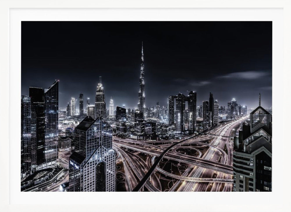 A striking black and white aerial photograph of the Dubai skyline at night, captured in a silver frame. The Burj Khalifa stands tall in the background, while a complex web of illuminated highway overpasses and light trails from traffic fills the foreground, creating a dynamic and futuristic cityscape. Print