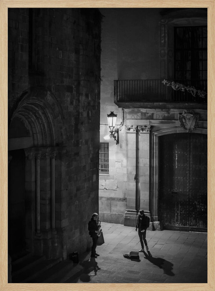 A high-angle, black and white photograph of a street musician playing a saxophone for a lone listener in a narrow stone alley at night. The scene is illuminated by an ornate streetlamp, casting long shadows on the cobblestone ground. Wall Art