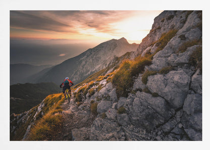 A mountain biker from behind rides along a narrow, rocky trail on a steep mountain ridge during a dramatic golden sunset. In the background, layers of mountains fade into the distance under a warm, glowing sky. Artwork