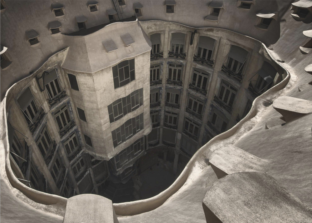 A surreal, high-angle photograph looking down into the distorted, cavernous courtyard of a building. The walls and windows appear to melt and curve inwards towards a dark void, creating a powerful optical illusion. The image has a muted, sepia-toned color palette and is presented in a silver frame. Wall Art