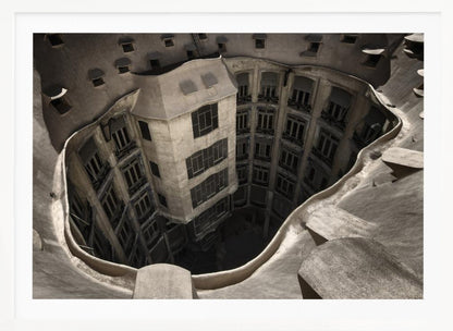 A surreal, high-angle photograph looking down into the distorted, cavernous courtyard of a building. The walls and windows appear to melt and curve inwards towards a dark void, creating a powerful optical illusion. The image has a muted, sepia-toned color palette and is presented in a silver frame. Wall Art