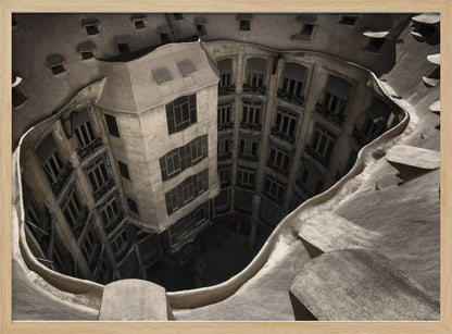 A surreal, high-angle photograph looking down into the distorted, cavernous courtyard of a building. The walls and windows appear to melt and curve inwards towards a dark void, creating a powerful optical illusion. The image has a muted, sepia-toned color palette and is presented in a silver frame. Wall Art