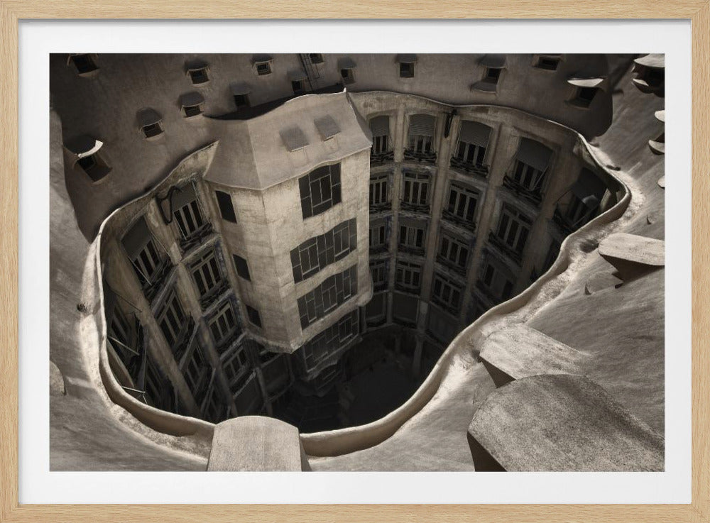 A surreal, high-angle photograph looking down into the distorted, cavernous courtyard of a building. The walls and windows appear to melt and curve inwards towards a dark void, creating a powerful optical illusion. The image has a muted, sepia-toned color palette and is presented in a silver frame. Wall Art