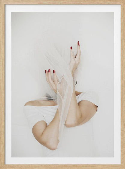 A minimalist photograph of a person in a white t-shirt against a white background, their face hidden by a sheer white veil. Their hands, adorned with bright red nail polish, frame the veiled face in an expressive pose. Wall Art