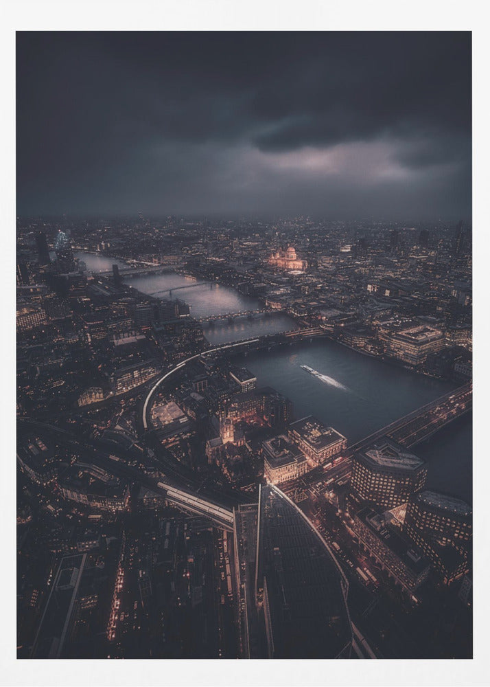 An aerial photograph of London at night from a high vantage point, overlooking the winding River Thames illuminated by the golden glow of city lights under a dark, dramatic, and cloudy sky. Wall Art