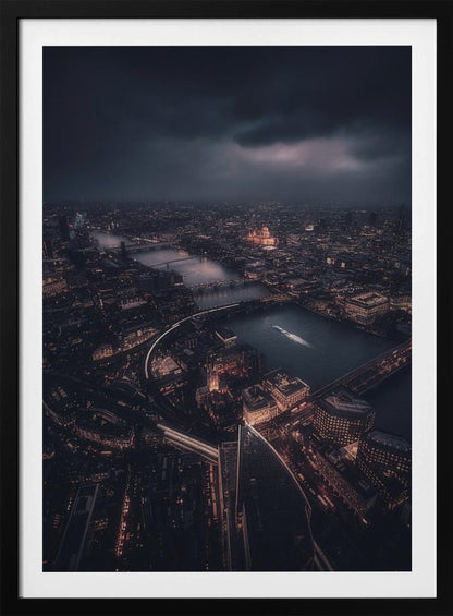 An aerial photograph of London at night from a high vantage point, overlooking the winding River Thames illuminated by the golden glow of city lights under a dark, dramatic, and cloudy sky. Wall Art