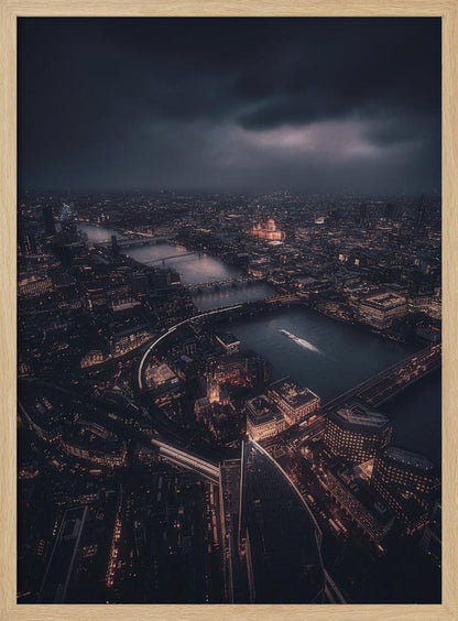 An aerial photograph of London at night from a high vantage point, overlooking the winding River Thames illuminated by the golden glow of city lights under a dark, dramatic, and cloudy sky. Wall Art