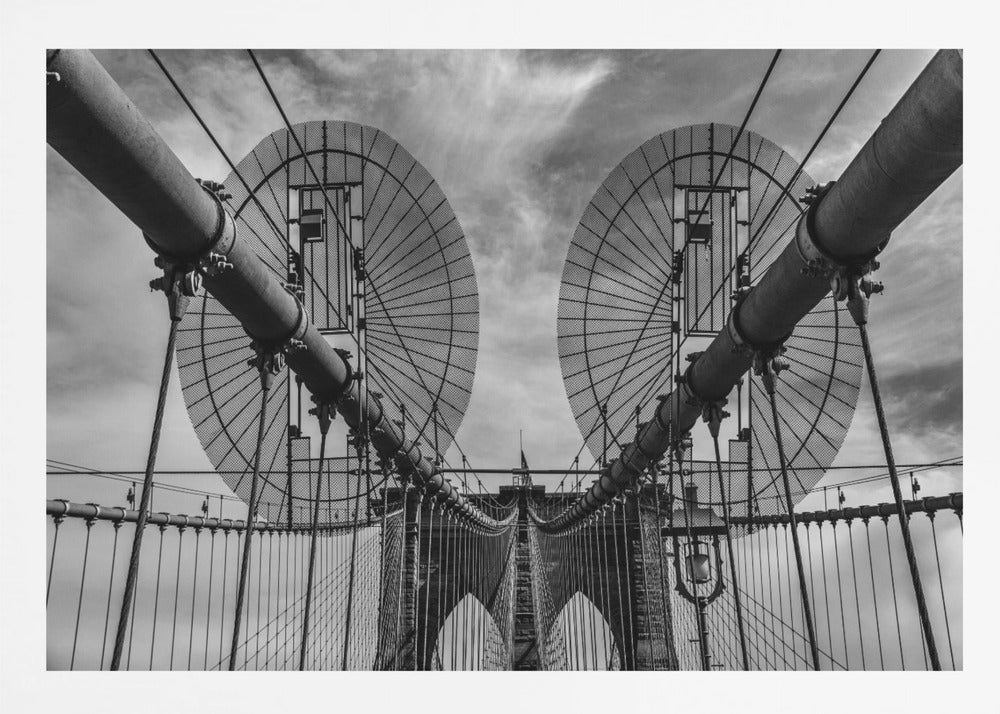 A symmetrical, low-angle black and white photograph of the Brooklyn Bridge's suspension cables and towers against a cloudy sky, framed in silver. Poster