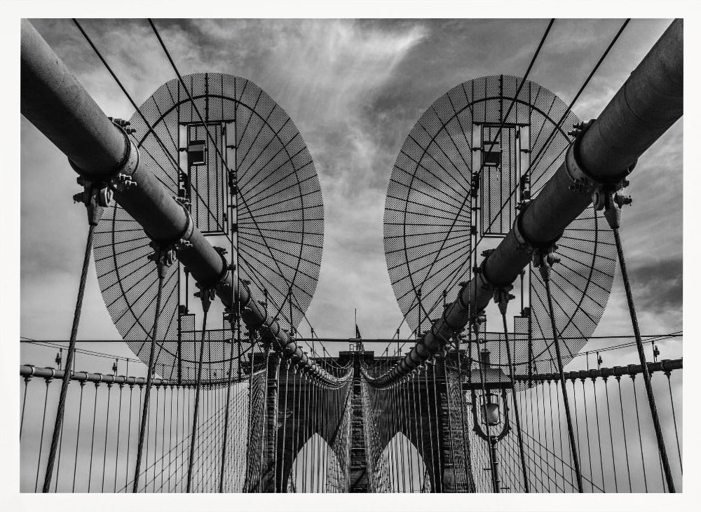 A symmetrical, low-angle black and white photograph of the Brooklyn Bridge's suspension cables and towers against a cloudy sky, framed in silver. Poster