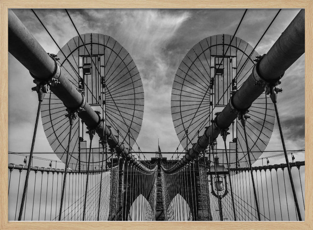 A symmetrical, low-angle black and white photograph of the Brooklyn Bridge's suspension cables and towers against a cloudy sky, framed in silver. Poster