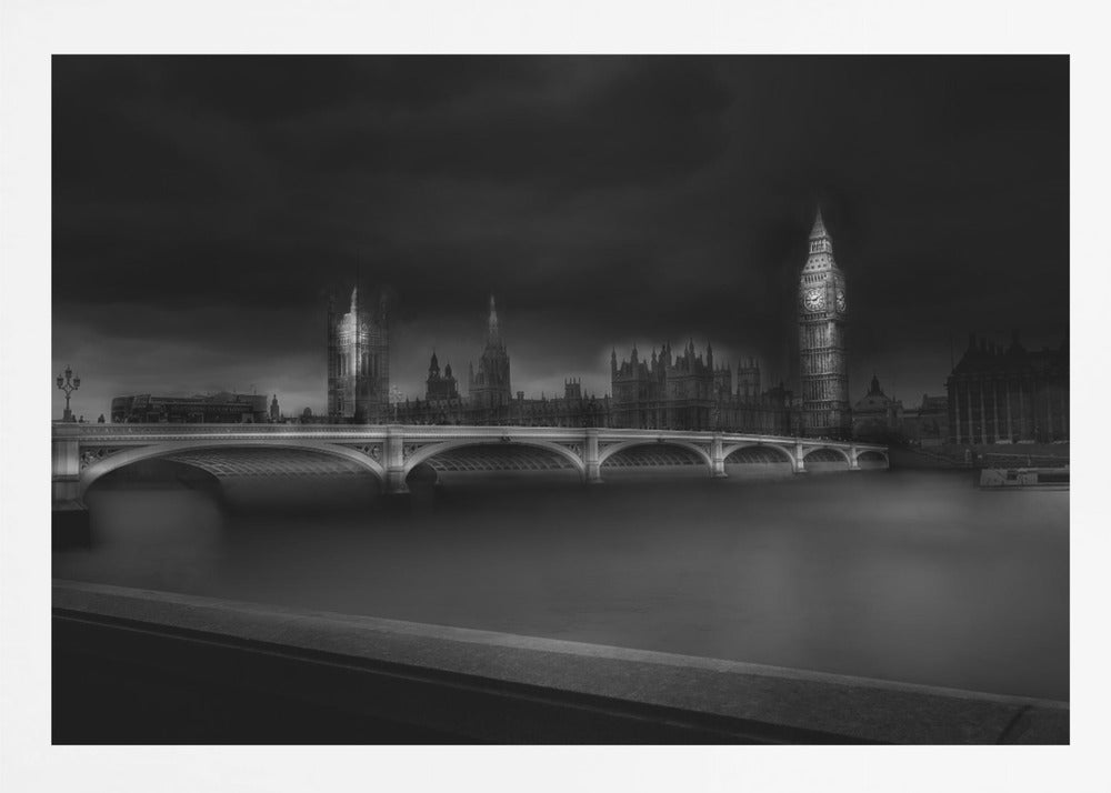 A moody, atmospheric black and white photograph of the Houses of Parliament and Big Ben in London, viewed from across the River Thames. The iconic buildings are softly illuminated against a dark, dramatic sky, with Westminster Bridge arching over the dark, smooth water in the foreground. The image is presented within a silver-colored frame. Artwork