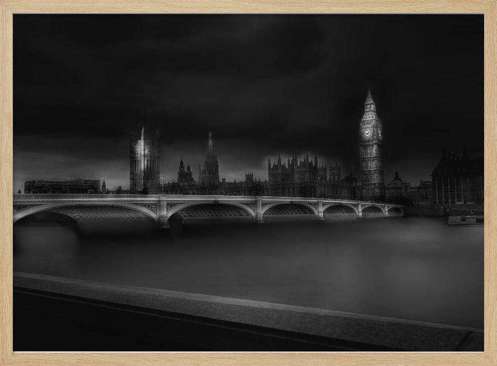 A moody, atmospheric black and white photograph of the Houses of Parliament and Big Ben in London, viewed from across the River Thames. The iconic buildings are softly illuminated against a dark, dramatic sky, with Westminster Bridge arching over the dark, smooth water in the foreground. The image is presented within a silver-colored frame. Artwork