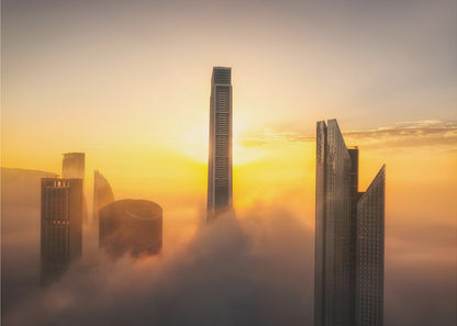 A framed photograph of a modern city skyline with skyscrapers emerging from a thick layer of clouds at sunrise, creating a dramatic and ethereal scene against a golden sky. Wall Art