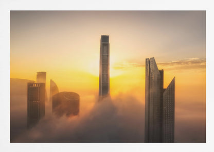A framed photograph of a modern city skyline with skyscrapers emerging from a thick layer of clouds at sunrise, creating a dramatic and ethereal scene against a golden sky. Wall Art